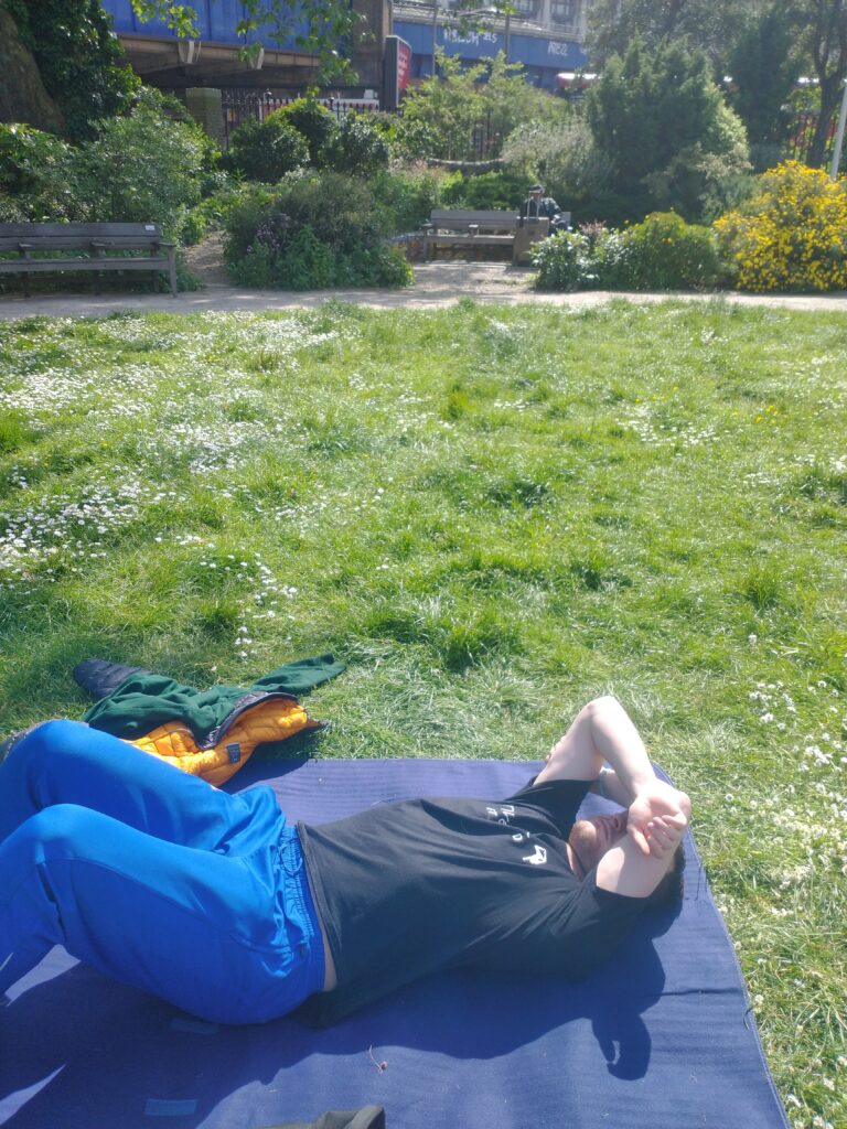 Alex lying in a sunny park covering his eyes with his arms.