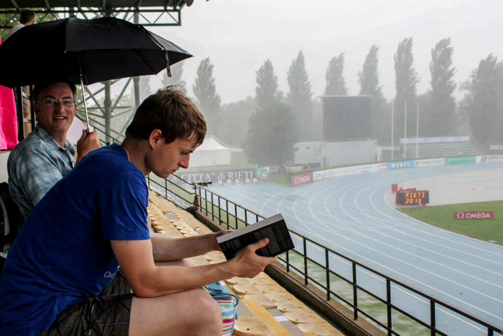 Alex sitting reading a book in an athletics stadium.